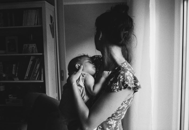 black white photo of woman breastfeeding nurturing baby looking away